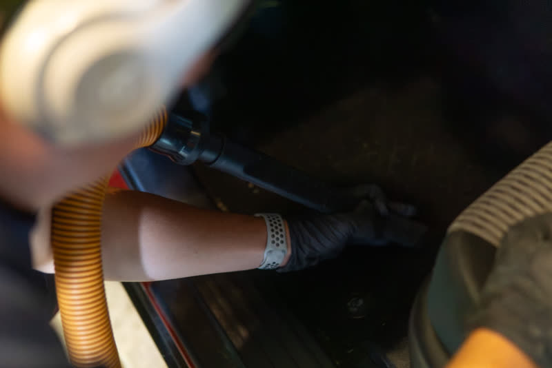 Vacuum nozzle and a gloved hand working the car floor